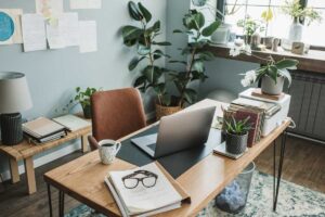 Office desk in Houston, TX, featuring a laptop, stacked books, and a small green plant.
